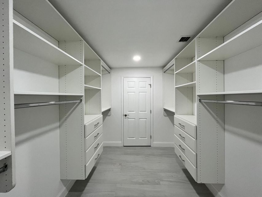 Walk-in closet with white shelving, drawers, and hanging rods on both sides, leading to a closed door.