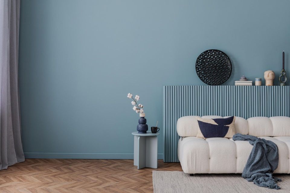 Minimal bedroom with blue wall, cream bed, round wall decor, and a small side table with flowers.