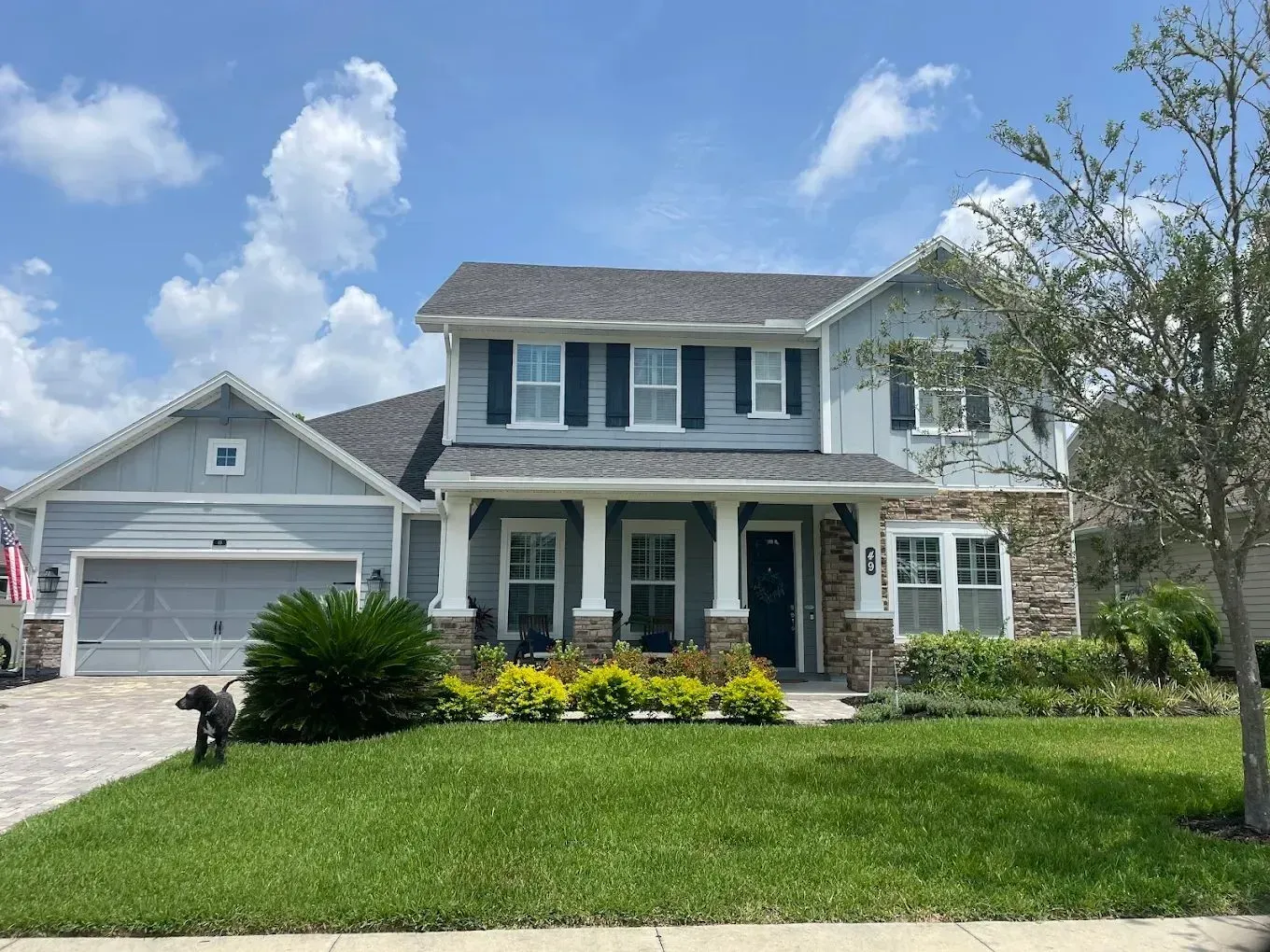 Suburban two-story house with gray siding, white trim, front porch, and a green lawn under a blue sky