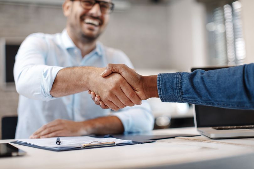 Handshake over a desk with a laptop and clipboard in an office setting