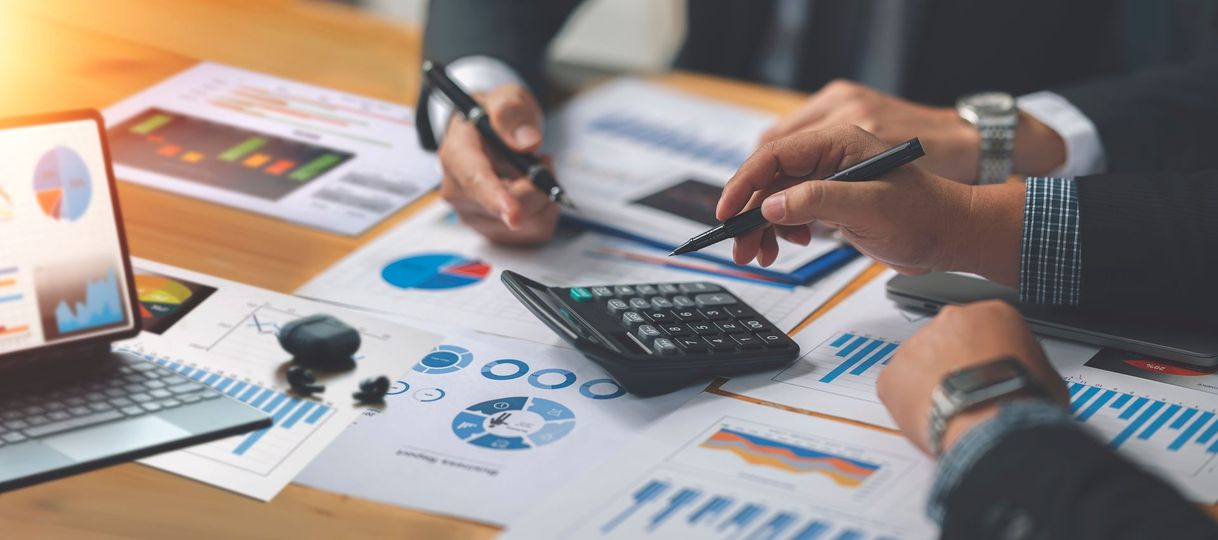 Hands using a calculator and pen over financial charts and reports on a desk