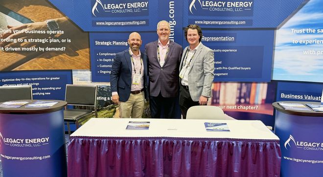 Dustin, Chad & Tyler standing at their Legacy Energy Consulting tradeshow booth with a table & blue branded banners.
