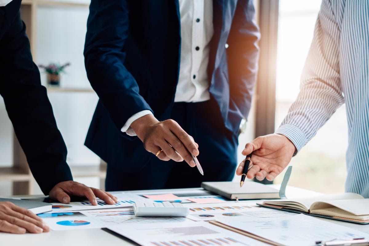 Two colleagues shake hands over a desk with charts and a calculator during a business sale discussio