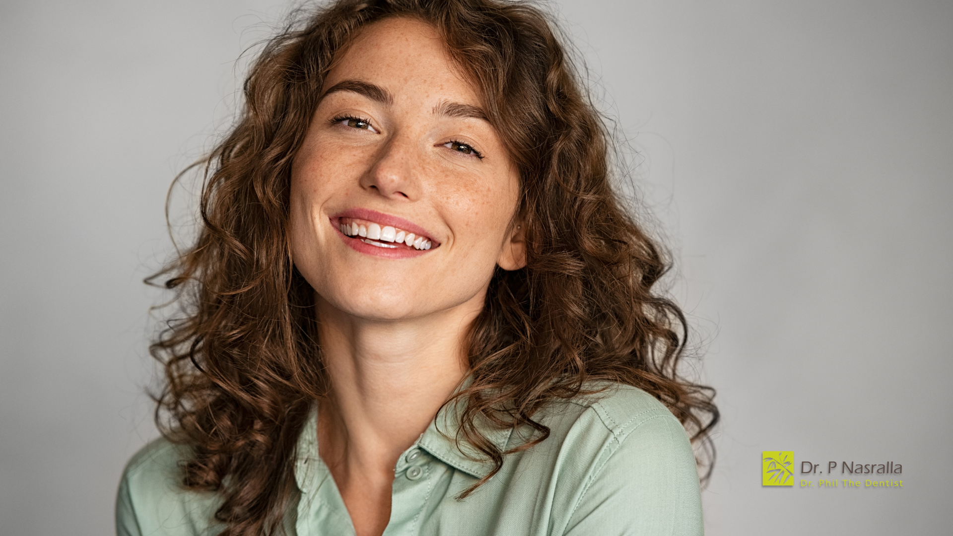 Smiling woman with curly brown hair against a light gray background, wearing a mint-green shirt.