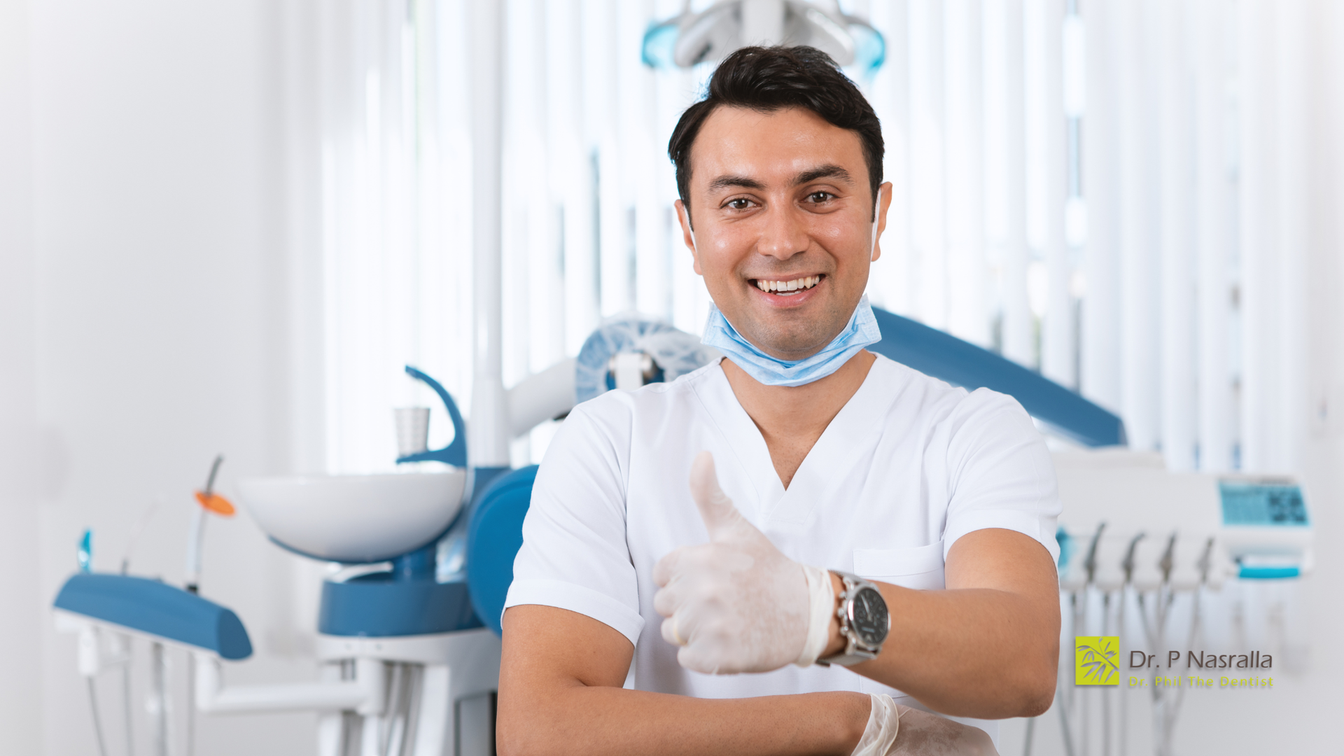 Dentist in white coat and gloves gives thumbs up in dental office.