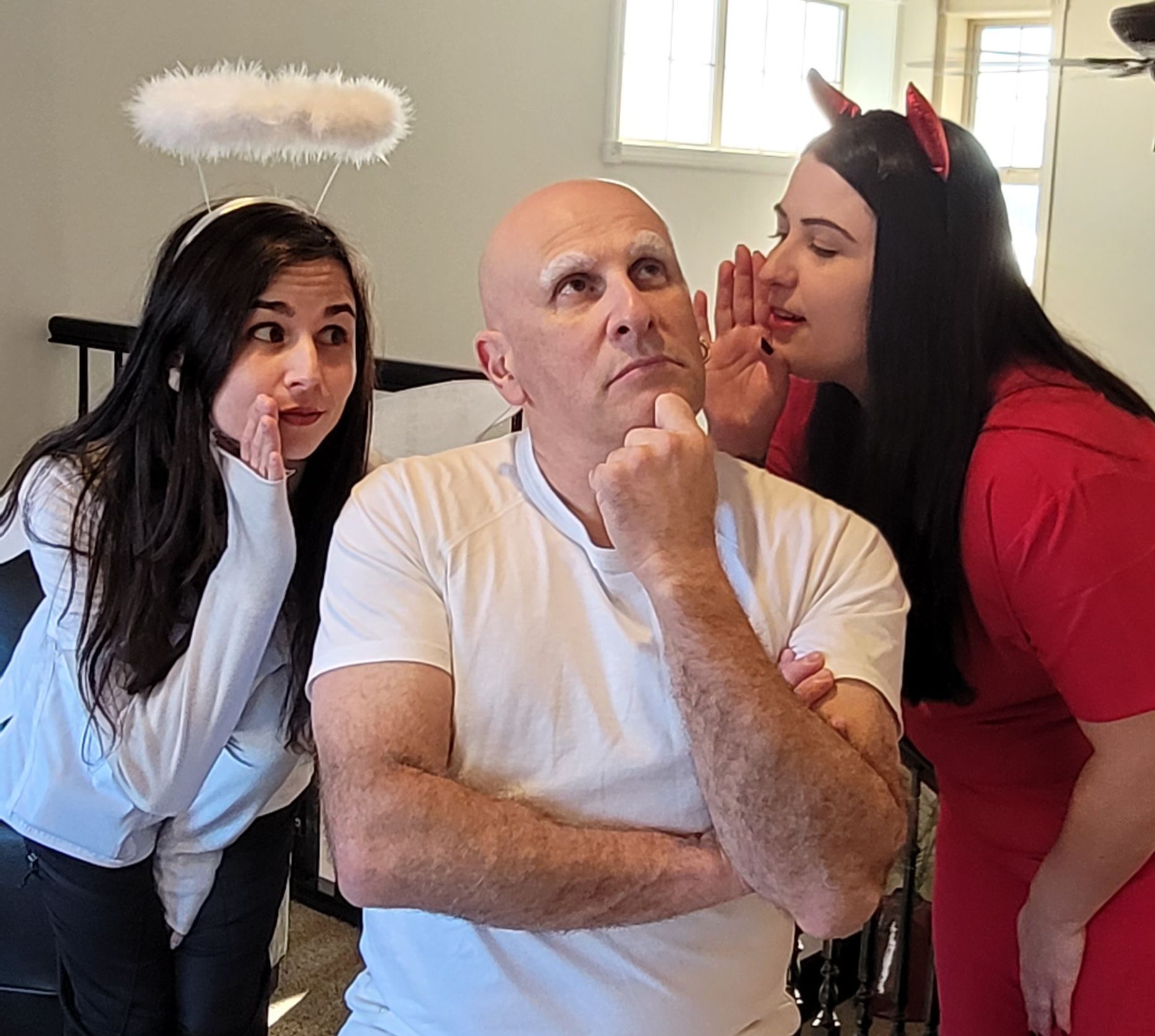A man in a white shirt looks contemplative as a woman in a halo whispers to his left and one in red horns to his right.