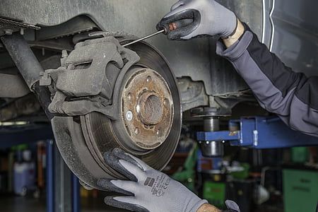 A mechanic in gray gloves uses a screwdriver on a car's brake system in an auto repair shop.