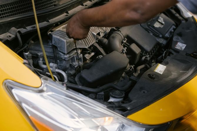 A hand checking the oil level in a yellow car's engine bay.