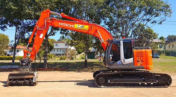 A large orange excavator is parked in a parking lot next to a smaller excavator.