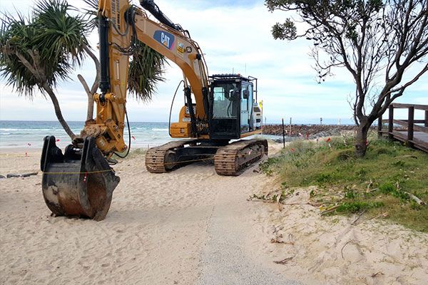 A large excavator is digging in the sand on a beach.