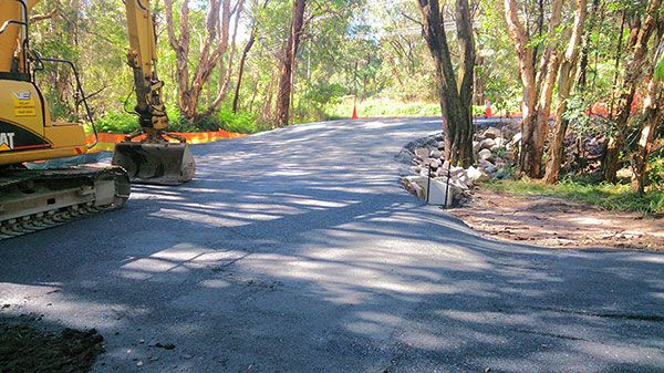 A yellow excavator is driving down a road in the woods.
