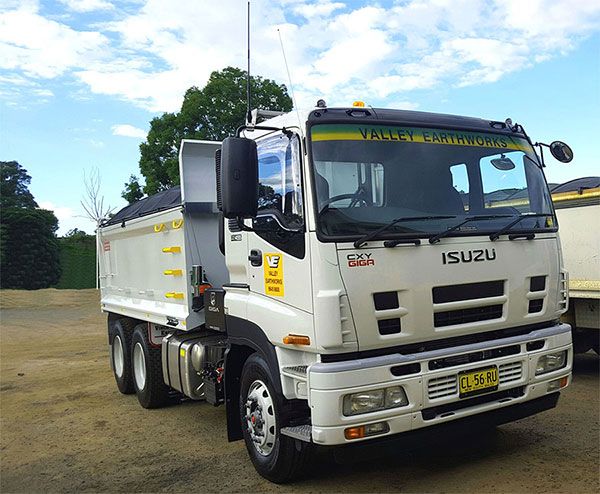 A white isuzu dump truck is parked on the side of the road.