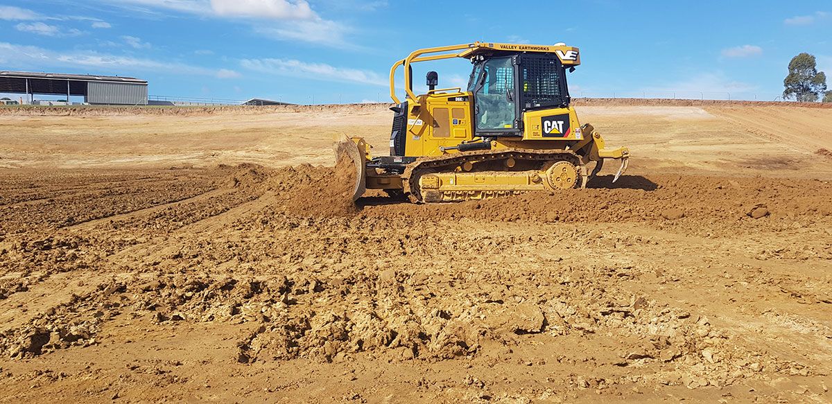 A yellow bulldozer is driving through a dirt field.