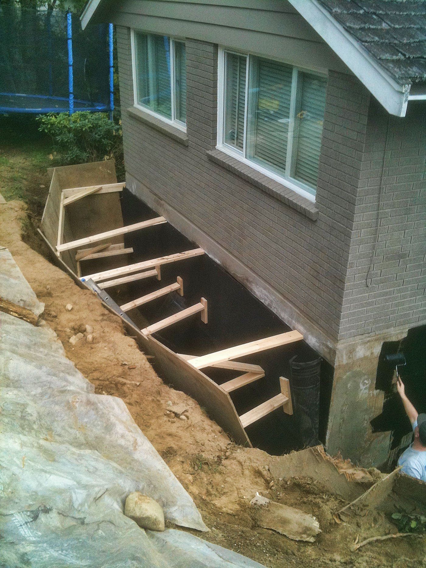 A wide trench dug around perimeter of home foundation to allow waterproofing material to be installed