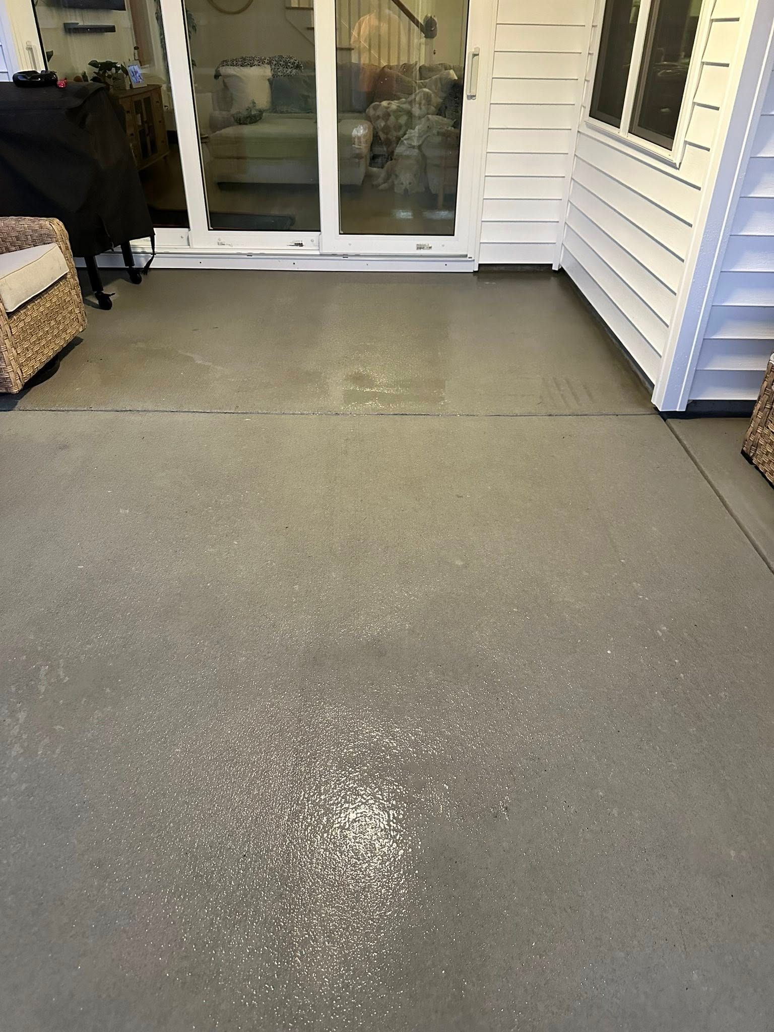 Patio with gray concrete floor, white siding, and sliding glass doors leading to a house interior