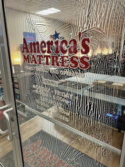 “America’s Mattress” storefront sign seen through a textured glass door in a retail shopping area