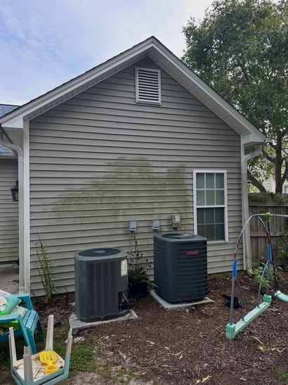Back of a gray house with two outdoor AC units and a window by a mulched yard