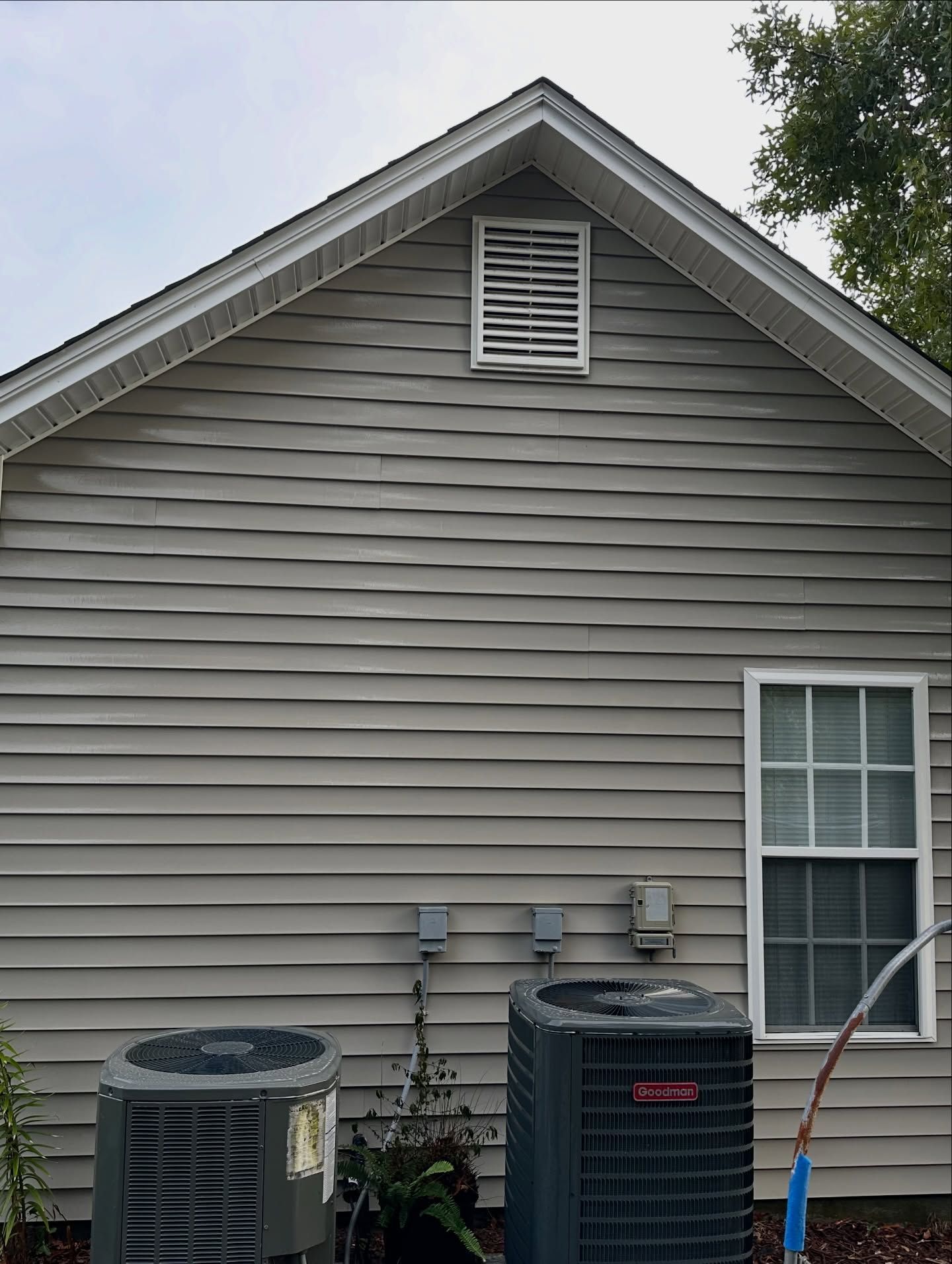 Side of a beige house with two outdoor HVAC units beneath a gable vent.