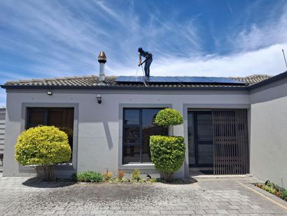 Worker on a roof over a gray house with trimmed bushes and a barred front door