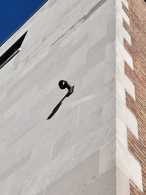 A modern building corner with a light fixture casting a shadow on the textured white wall.
