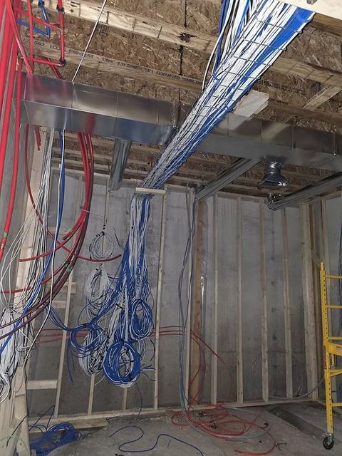 Electrical and plumbing infrastructure under construction, with hanging blue and red wires.