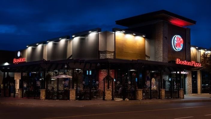 Boston Pizza restaurant exterior at night. Lit signage, outdoor patio, dark sky.