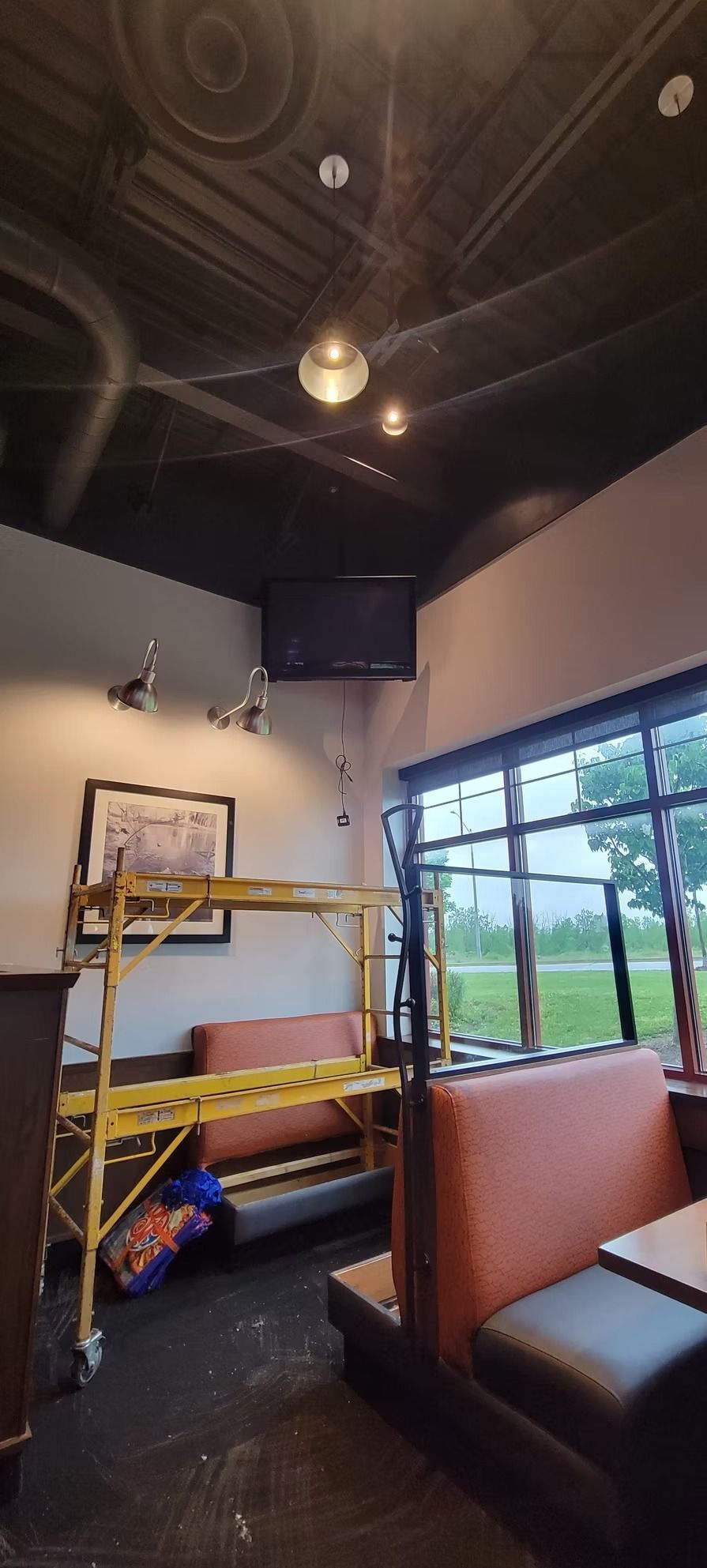 Interior of a restaurant with booth seating, a television, and a yellow scaffold.