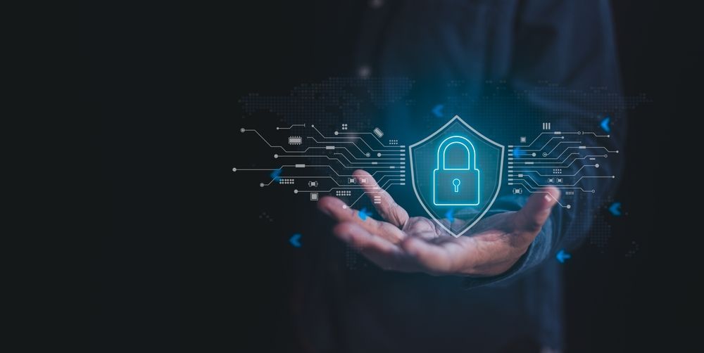 Person's hand holding a glowing shield with a padlock. Digital security concept in blue on a dark background.