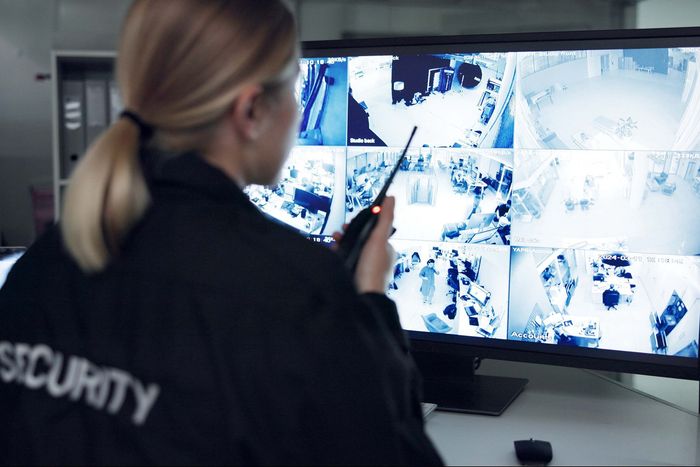 Security guard in black uniform monitors surveillance screens.