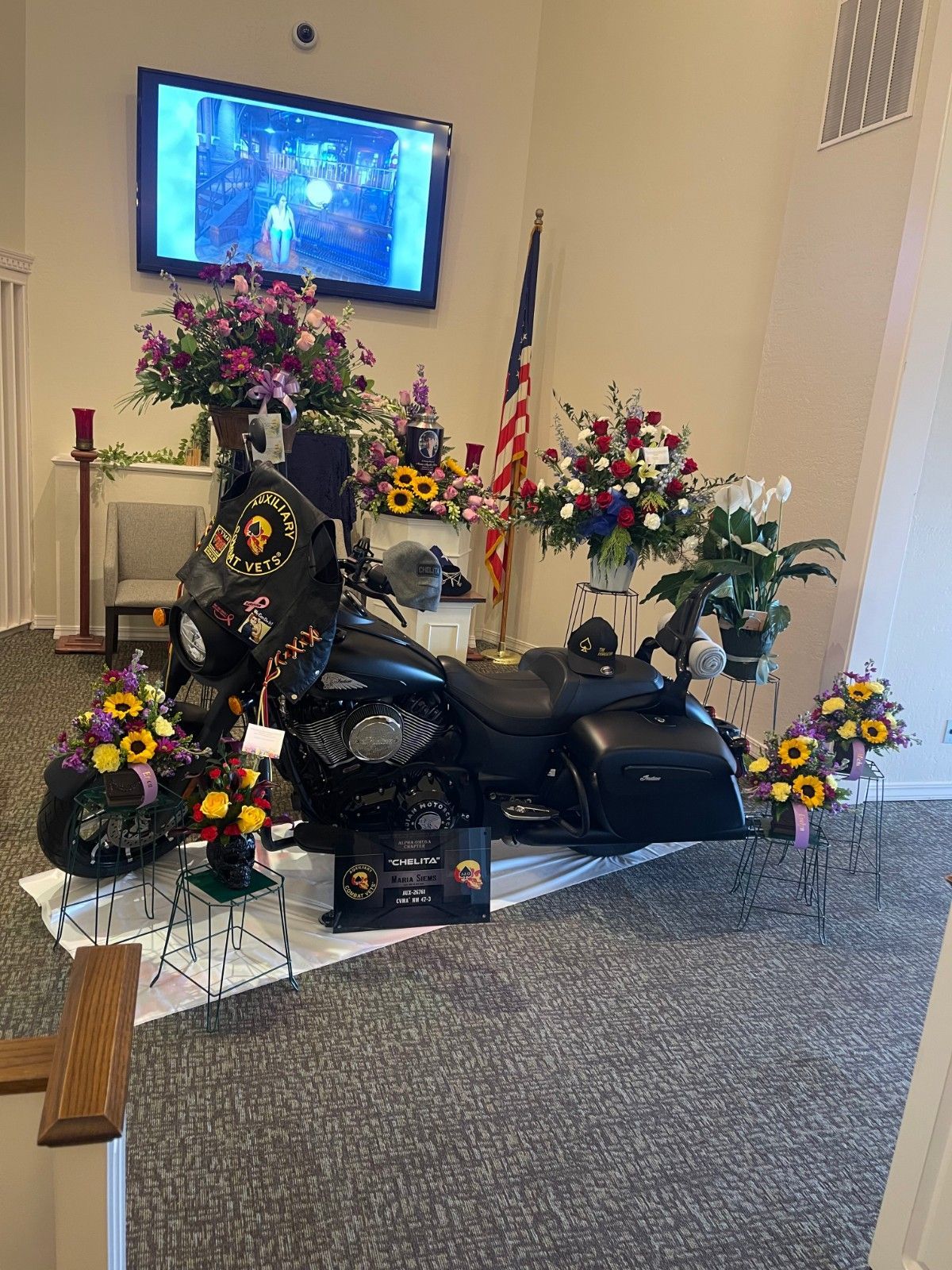 Motocross bike with helmet on seat, wooden urn, floral arrangement, and trophy, part of a cremation with memorial display