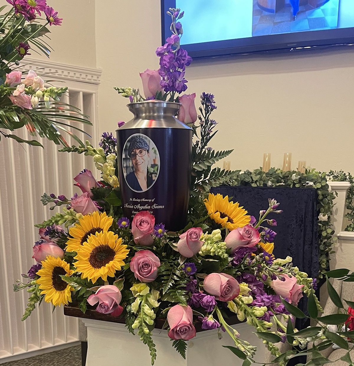 Close-up of cremation urn with portrait surrounded by wreath, displayed with personal American flag and keepsakes in a personalized memorial tribute