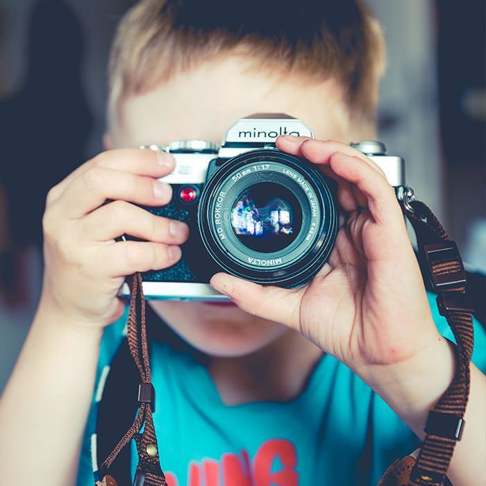 A young boy is taking a picture with a minolta camera