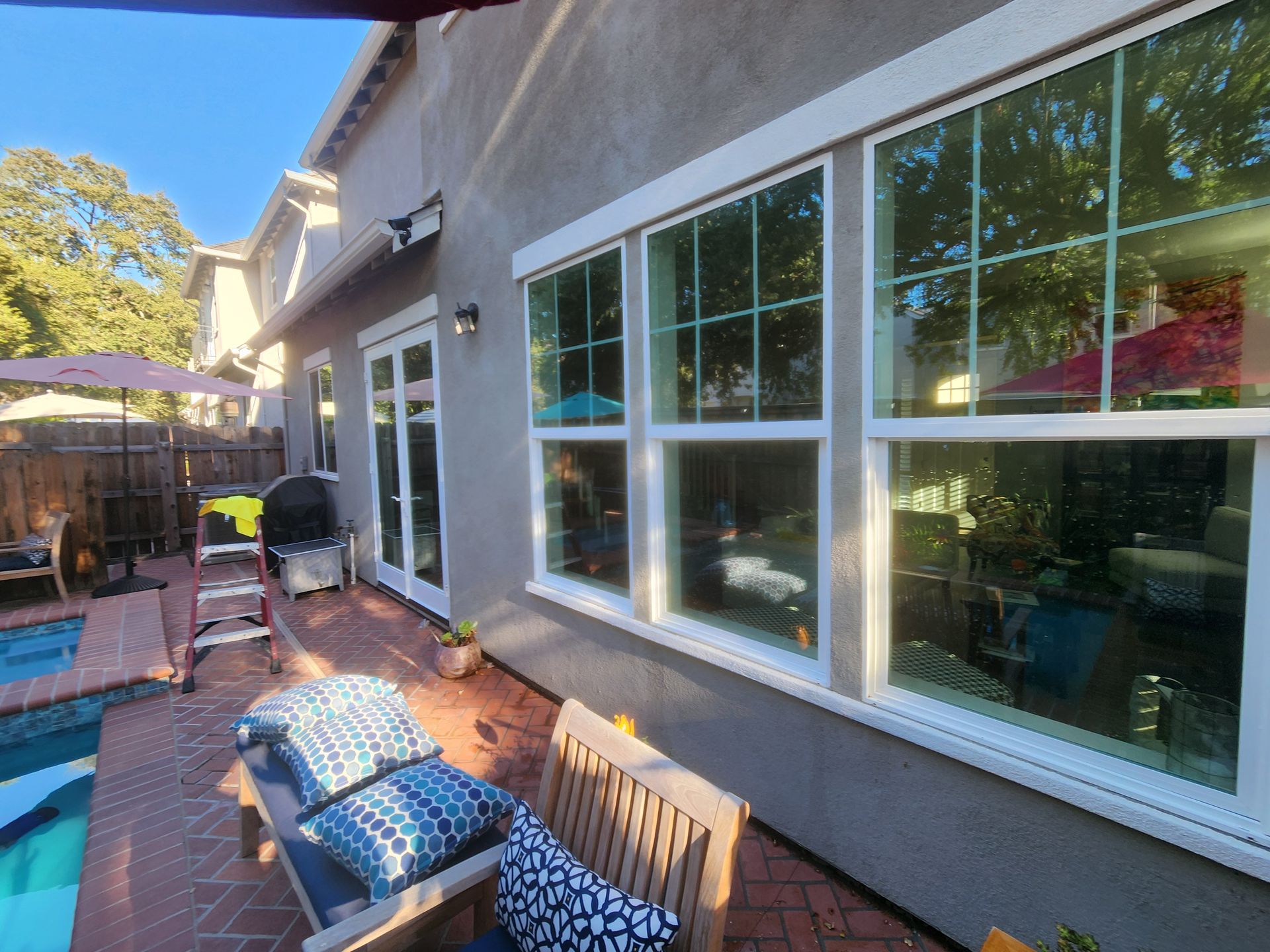 Back patio with lounge chairs, brick floor, and large windows along a house exterior