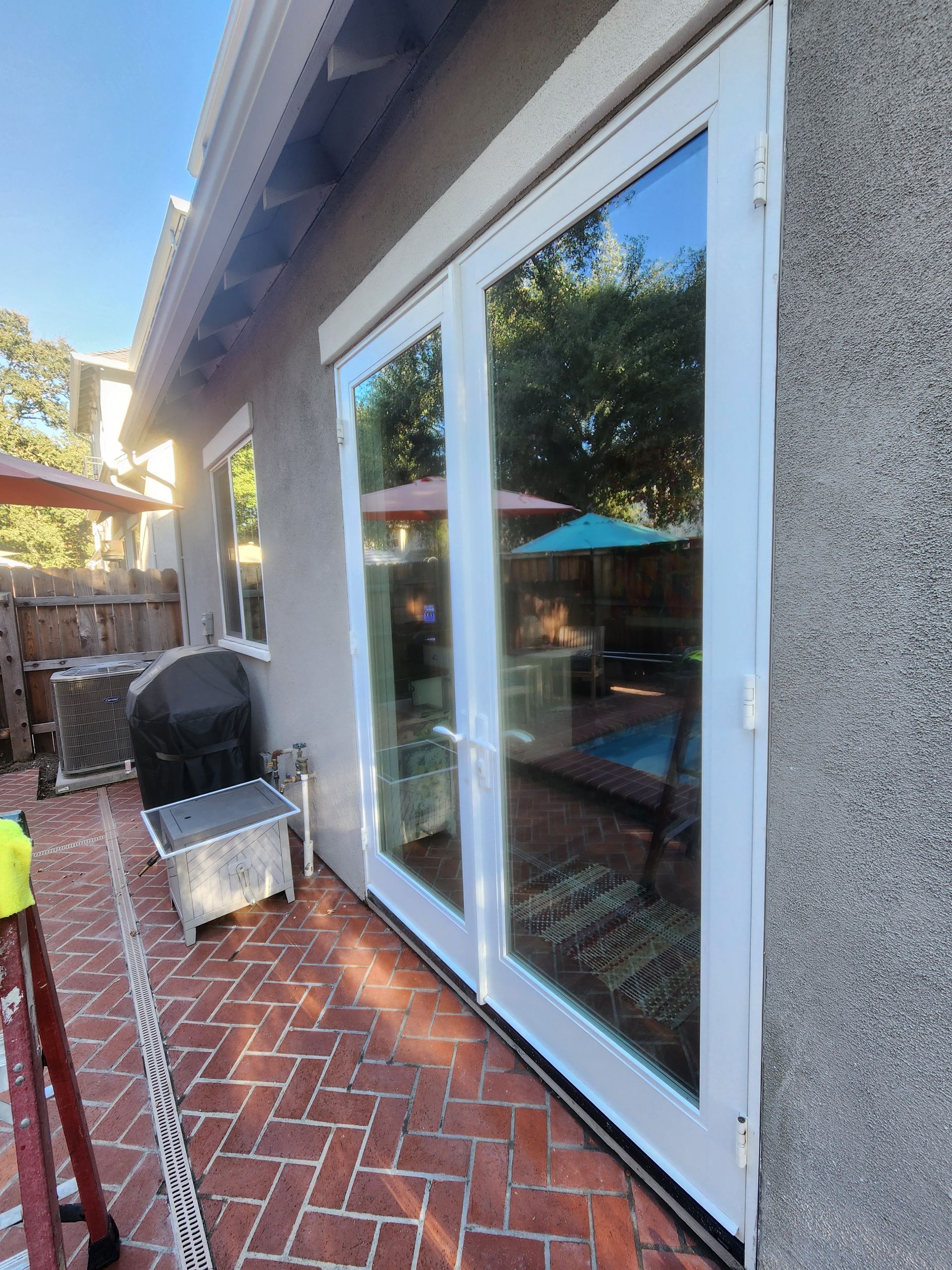 Patio with brick floor, white sliding glass doors, and a barbecue grill beside a stucco wall.