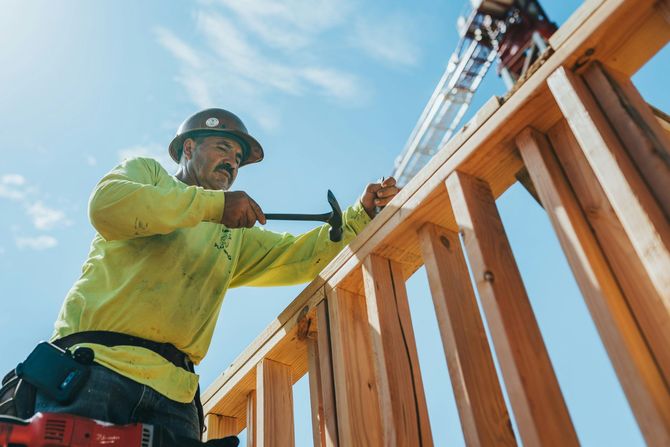 Construction worker hammering wooden framing against a bright blue sky