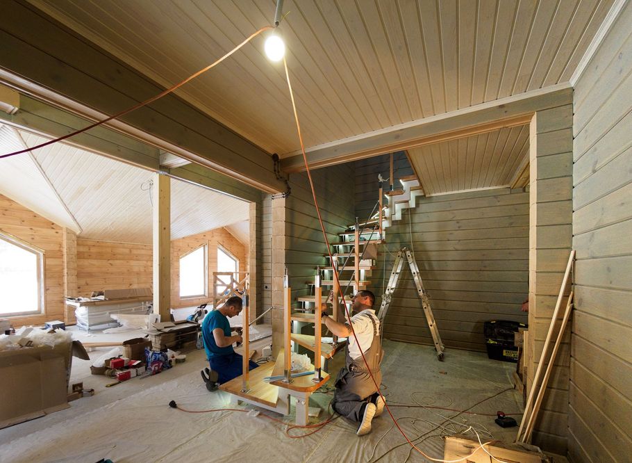 Two people working in an unfinished wooden room with a staircase under construction.