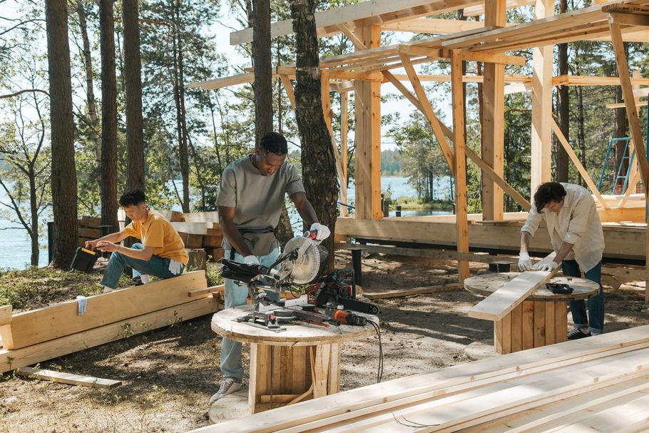 Three people assembling wooden frames at an outdoor construction site in a pine forest