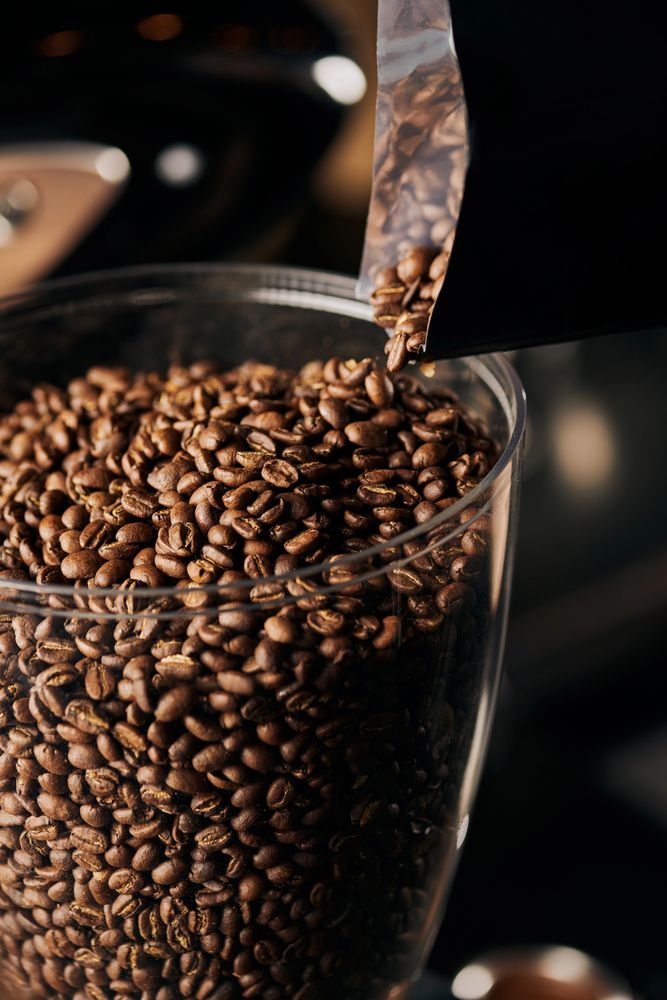 Chicchi di caffè versati da un sacchetto in un contenitore trasparente per macinare.