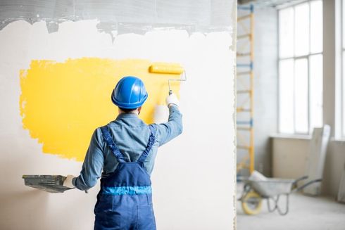 Worker painting a white wall yellow in a bright room under renovation