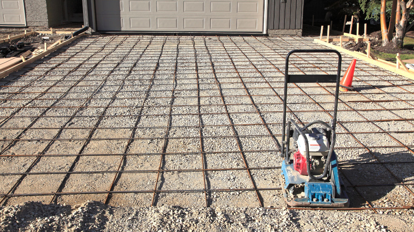 A vibratory plate is sitting on top of a concrete driveway.