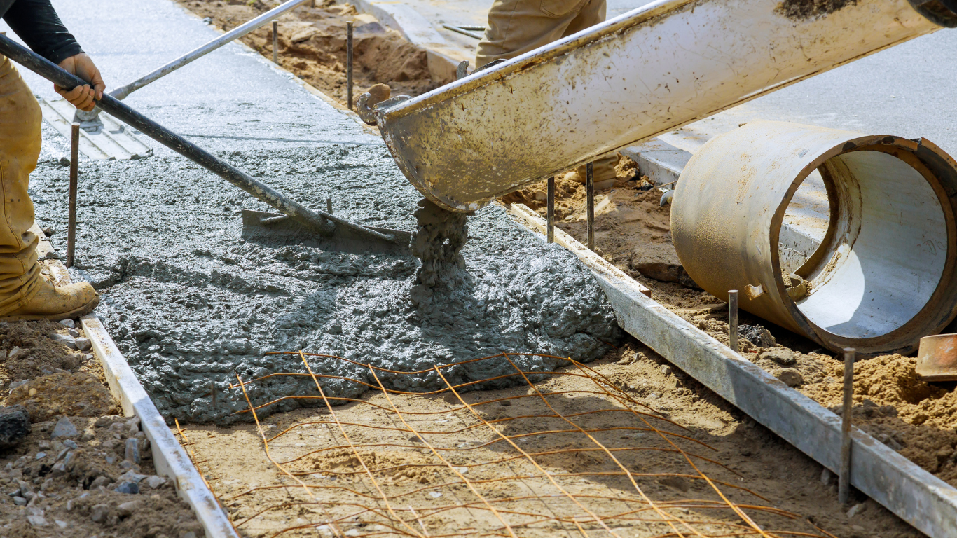 A man is pouring concrete on a sidewalk with a shovel.