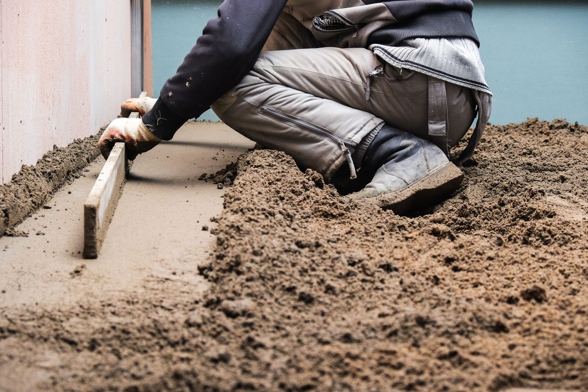 A man is kneeling on the ground using a level to level concrete.