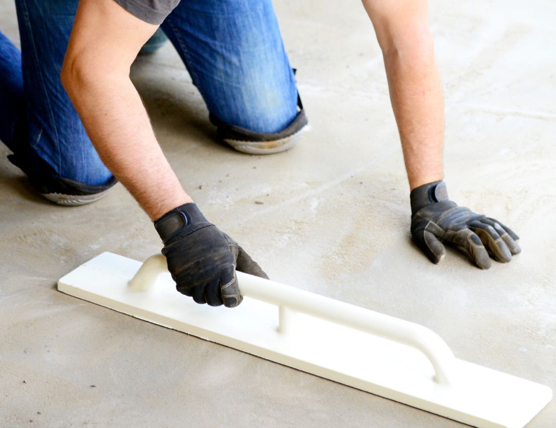 A person wearing gloves is using a trowel on a concrete floor