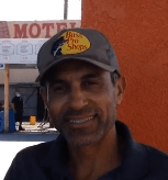 A man wearing a baseball cap is smiling in front of a motel.