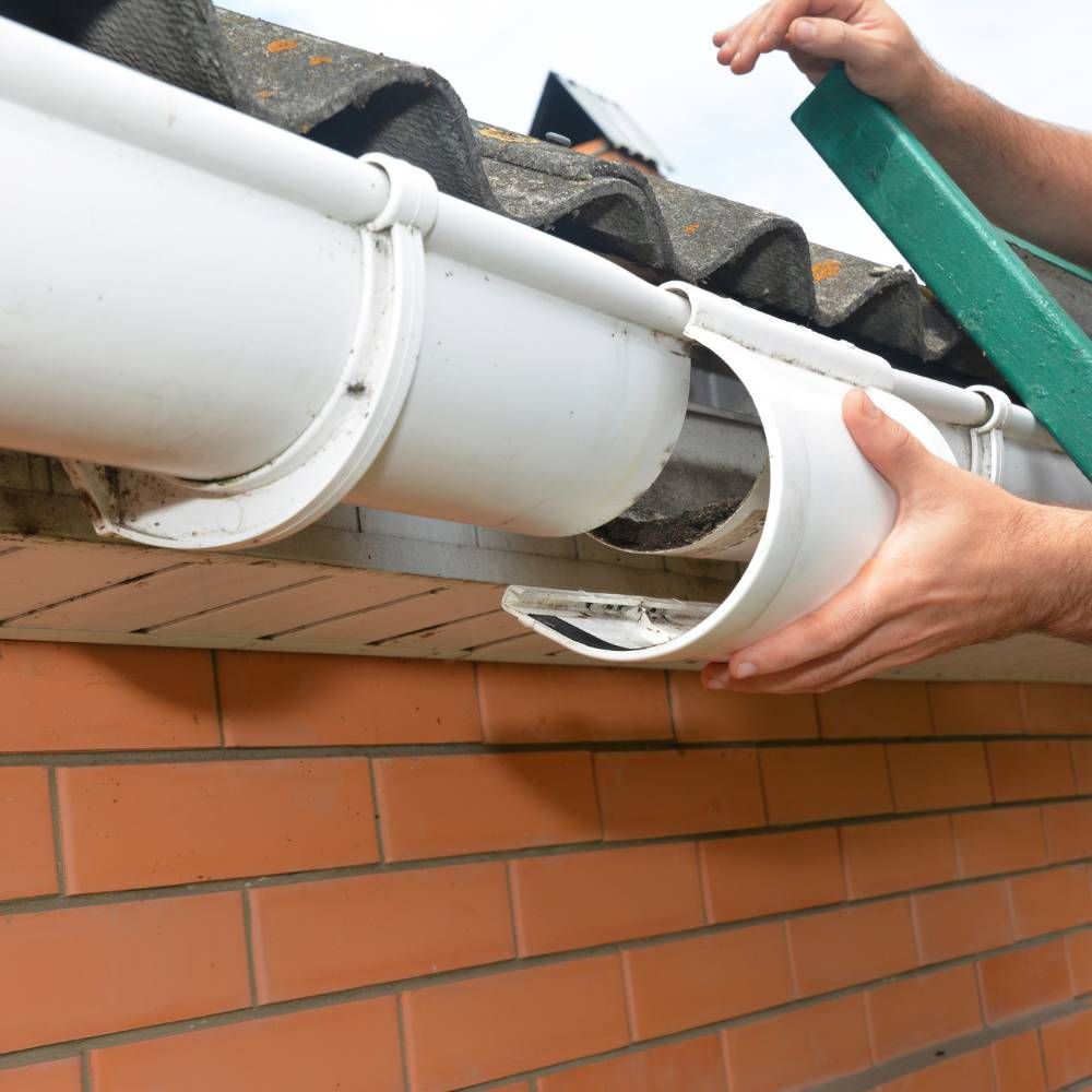 A person is fixing a gutter on a brick wall.