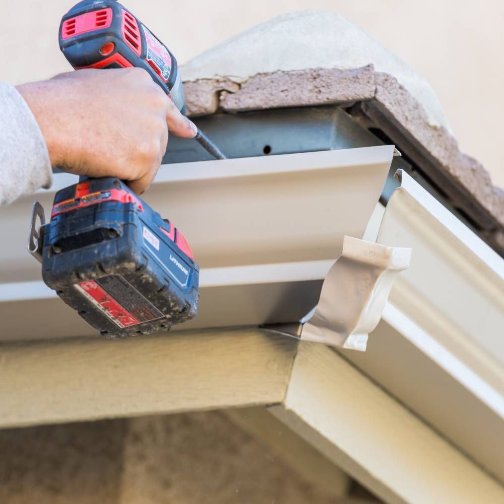 A person is working on a gutter with a cordless drill