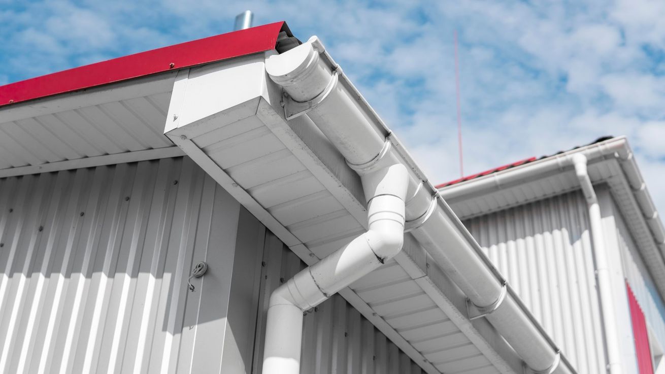 A white gutter on the side of a building with a red roof.