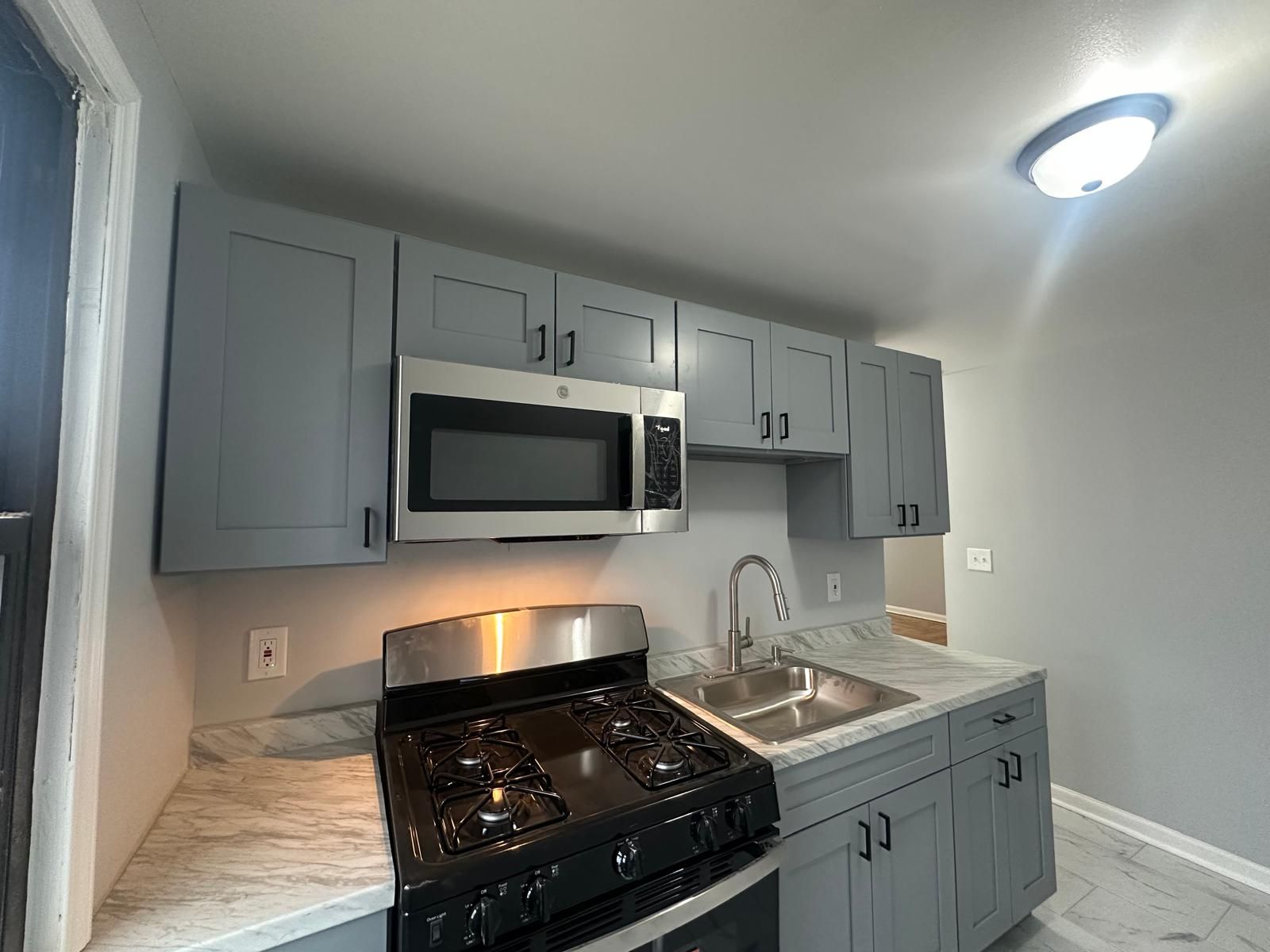 A small, modern kitchen with gray cabinets, stainless steel appliances, and light countertops.