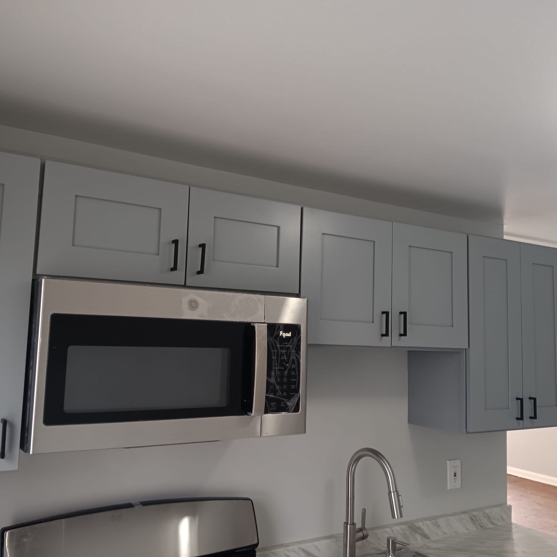 Kitchen cabinets are gray, with black handles, and stainless steel microwave and sink.