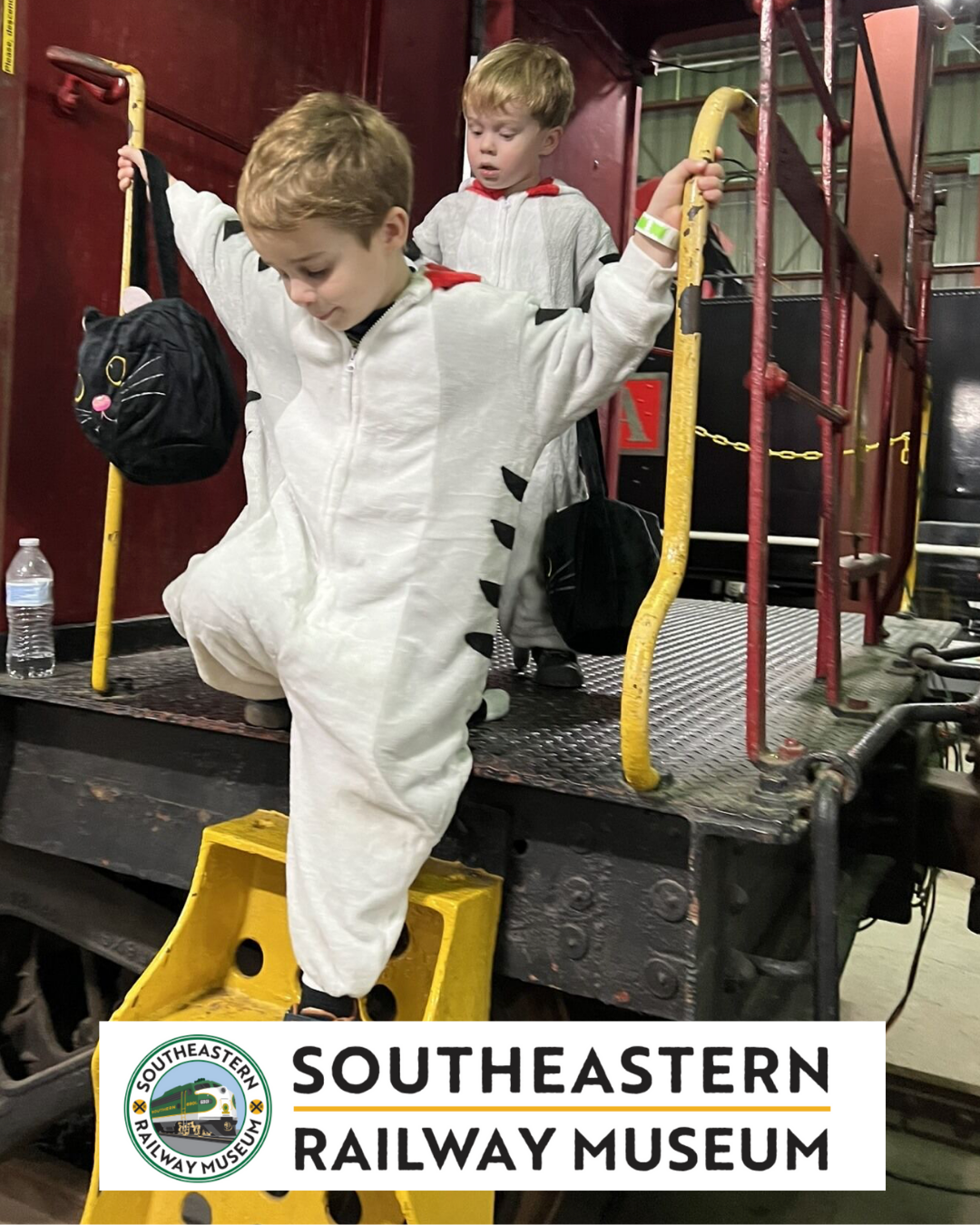 Two children in white animal costumes climb aboard a train at the Southeastern Railway Museum.